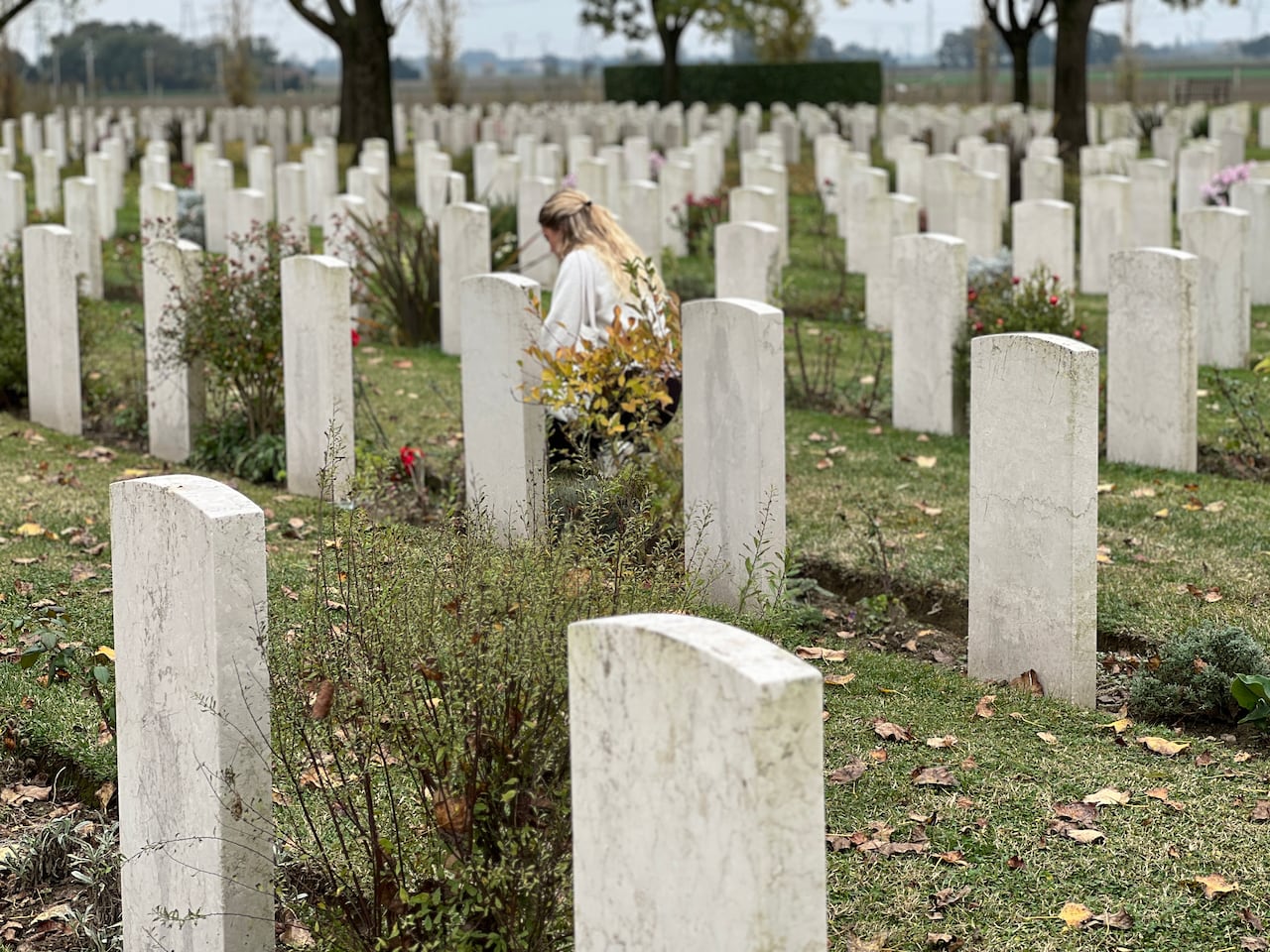 A young woman with blond hair lays flowers at a military cemetery in Italy.