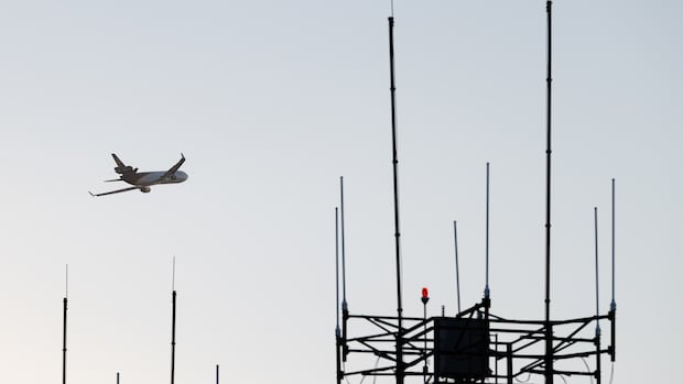 A plane flies in the sky as an air traffic control tower is seen in the foreground
