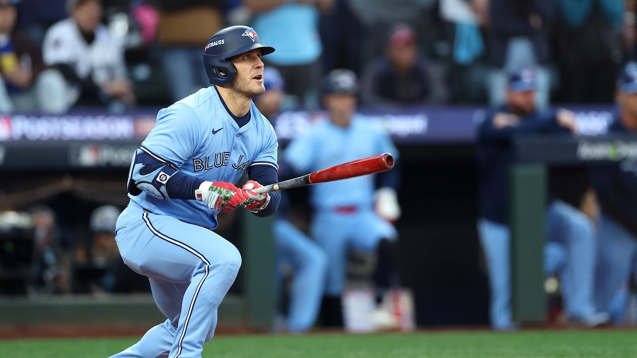 A man in a blue baseball uniform holds a bat and looks upward.