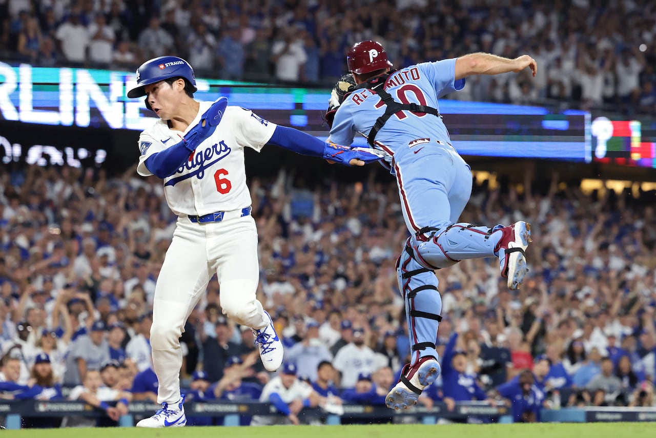 A baseball player cringes as he crosses home plate to score while a catcher is shown in mid-air trying to catch a ball.