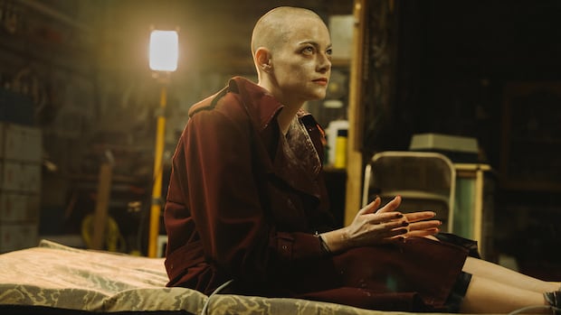 Emma Stone appears in a scene from Bugonia. The Yorgos Lanthimos-directed comedy charts the story of a man convinced a local CEO is an alien in disguise. A bald woman in a robe is shown tied to a thin mattress. She is in a basement with an industrial light behind her.