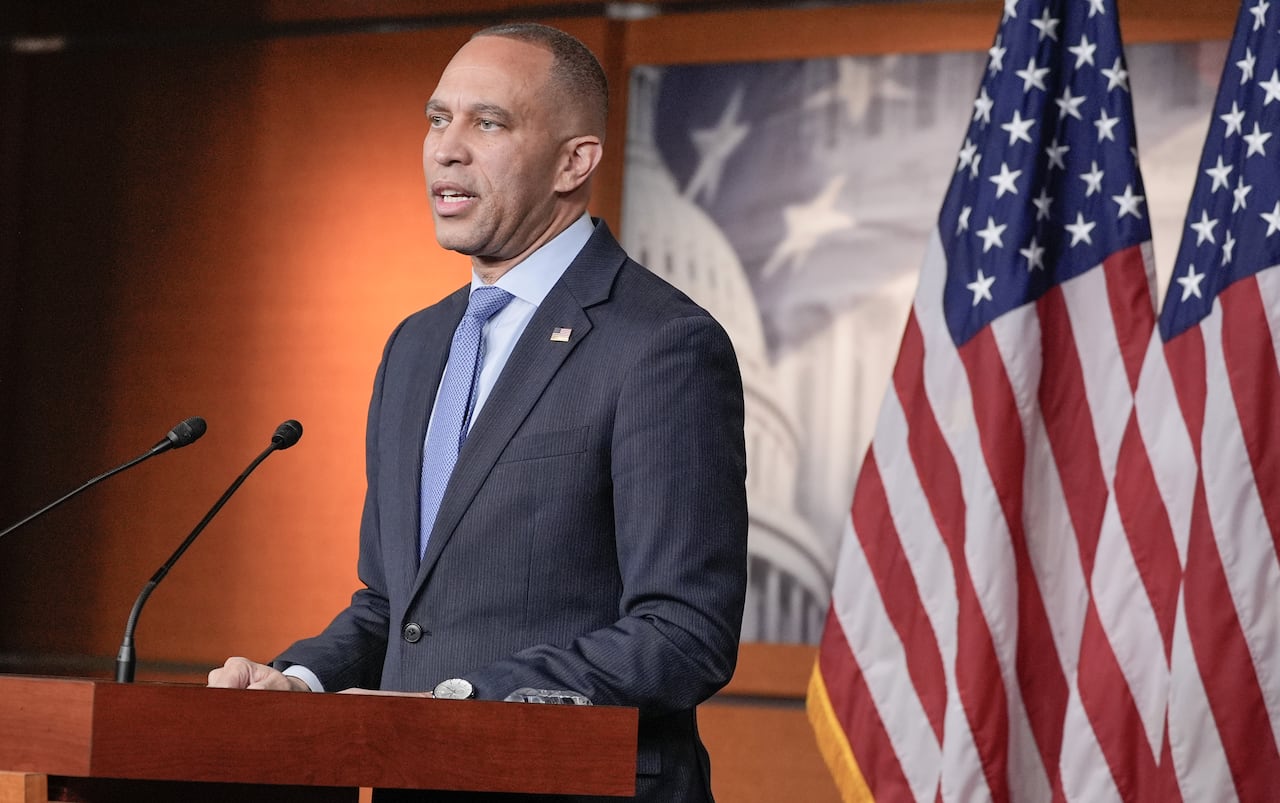 Hakeem Jeffries stands at a podium with a pair of U.S. flags in the background. 