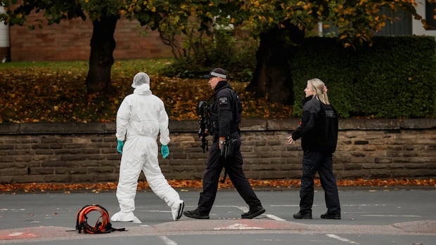 A forensic technician and police officers work at the scene after a man drove a car into pedestrians and stabbed a security guard in an attack at a synagogue where worshippers were marking Yom Kippur, the holiest day on the Jewish calendar, according to the British police, in north Manchester, Britain, October 2, 2025. REUTERS/Phil Noble Police officers stand next to a person in a white hazmat suit.