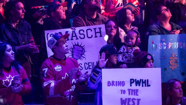 Fans hold up signs at a hockey game, declaring they would like the PWHL to come to the west coast.