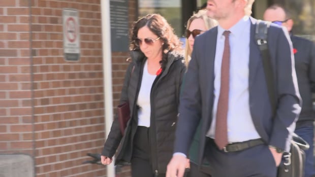 Woman in sunglasses, black jacket with poppy leaving a courtroom