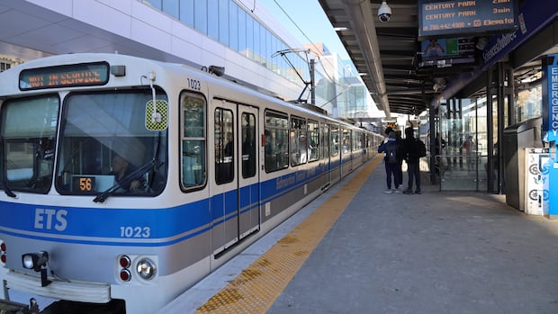 An Edmonton LRT train on the platform at Health Sciences station. A white and blue LRT train sits on an outdoor platform with people walking in the background.