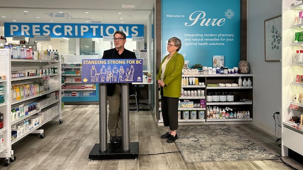 Dr. Martin Lavoie, deputy provincial health officer, speaks with B.C. Health Minister Josie Osborne Oct. 22, 2025 to urge British Columbians to get their vaccinations during flu season. A man speaks at a podium in a pharmacy while a woman stands beside him