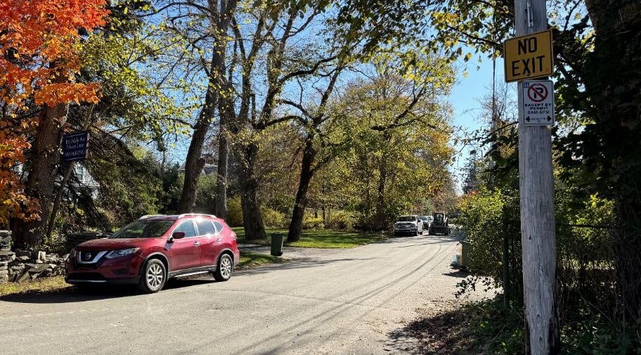 Cars are parked on a street with many trees, some in orange fall colours. A blue sign says private lane, no parking