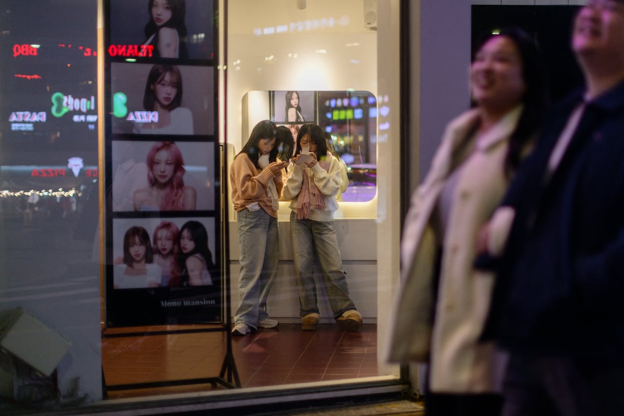 Two young woman huddle near a photo booth looking at their strips.