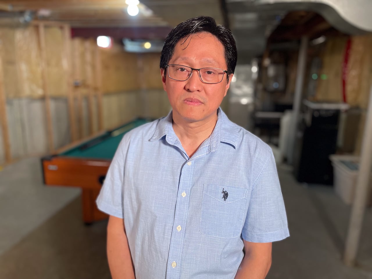 A man stands in an unfinished basement. He looks unhappy.