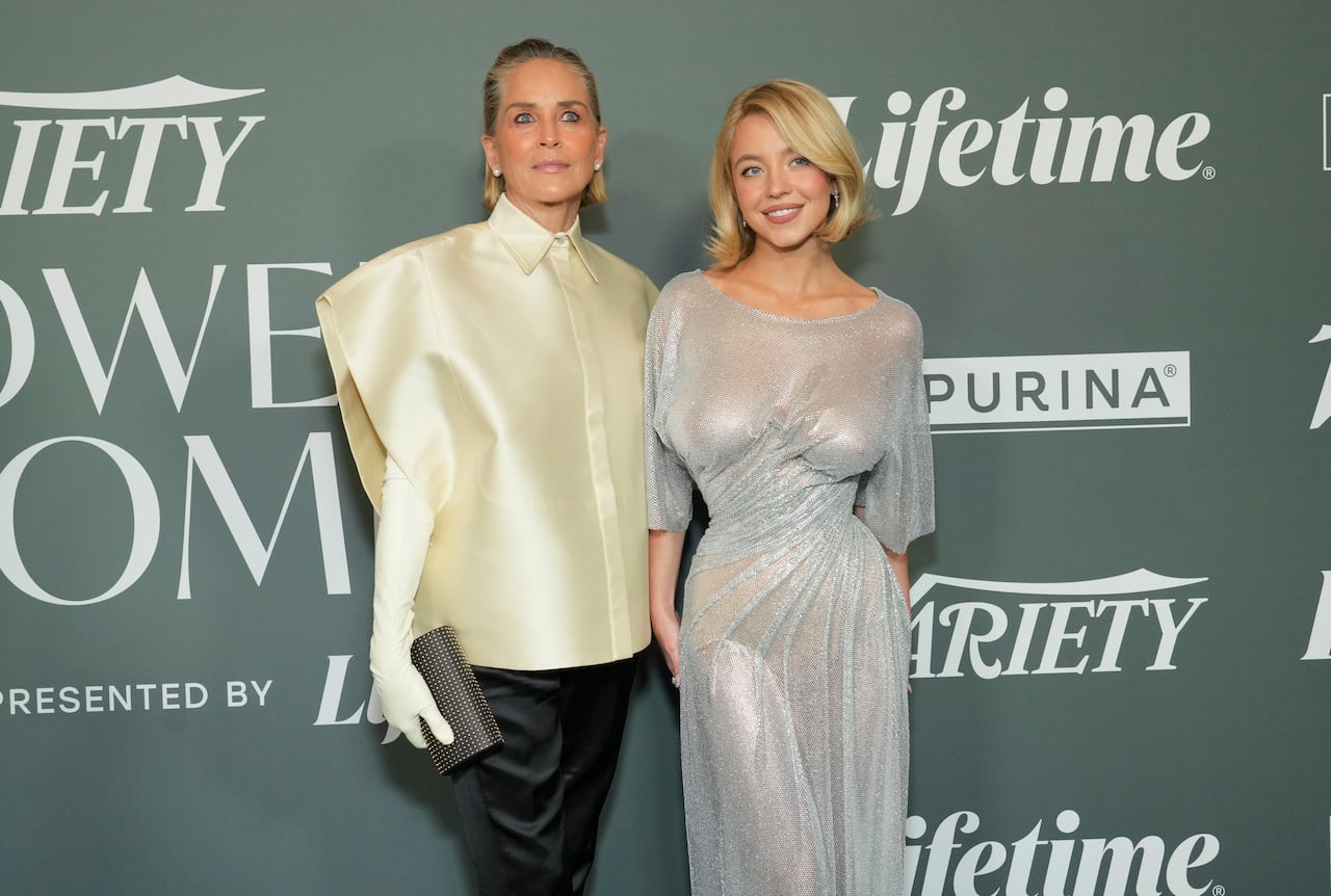 A woman in a silky yellow shirt and a woman in a sheer silver dress pose together.