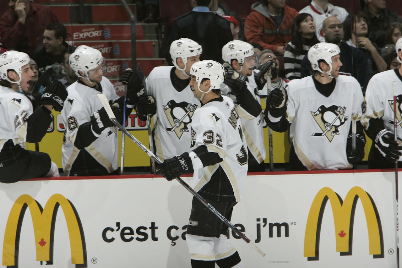 A hockey player is shown celebrating a goal with his teammates on his bench.