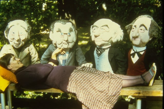 A woman lies on a wooden bench. Behind her are four, large soft sculptures of Canadian prime ministers.
