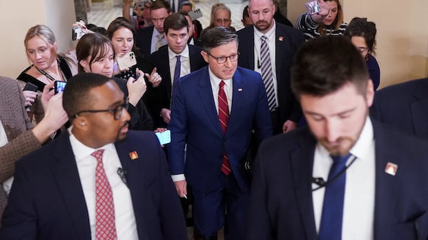 A group of people, some in suits, walk down a hallway