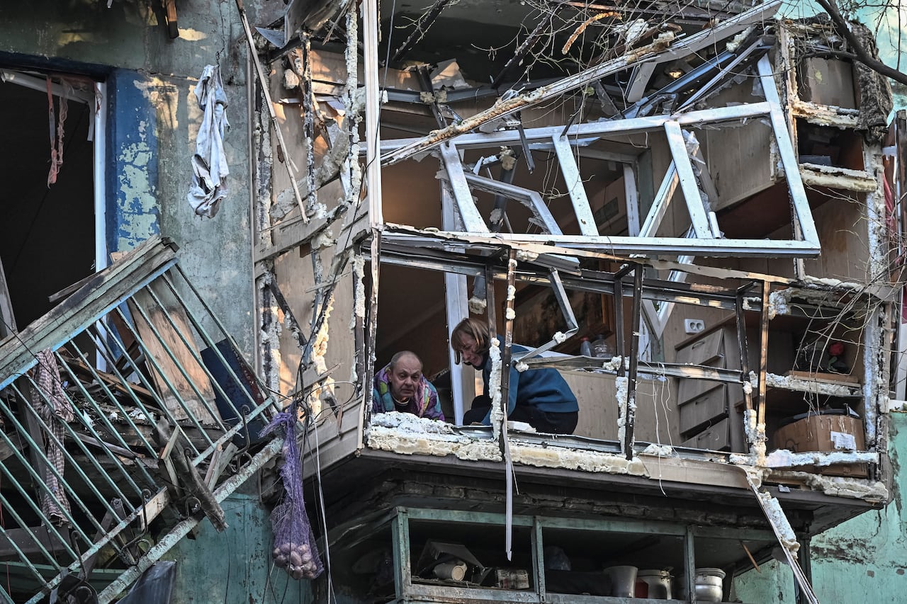 A man and woman are shown on the mangled balcony of a severely damaged apartment building.