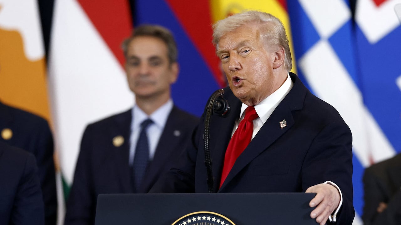 Donald Trump stands in front of podium, mouth open to signal speech