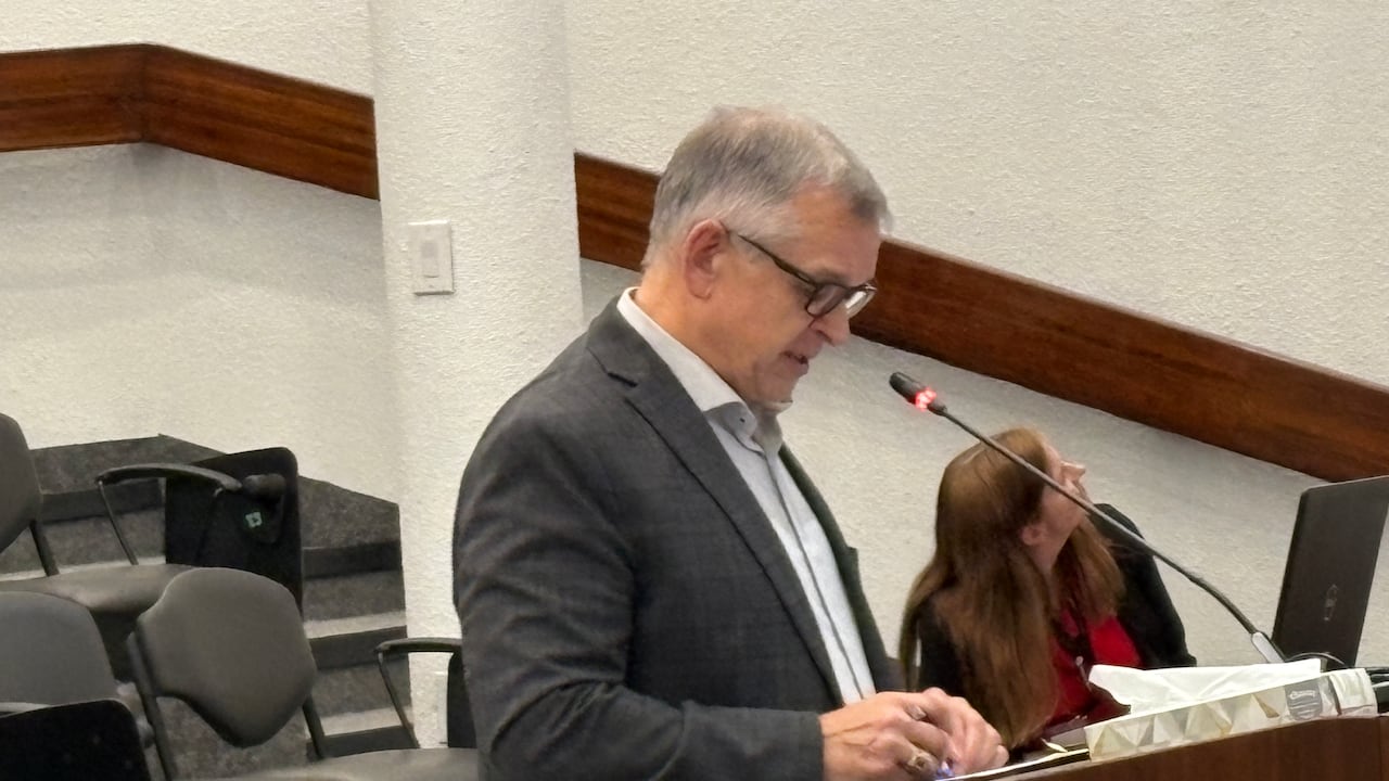 Man, speaking at a podium mic, pictured from side.