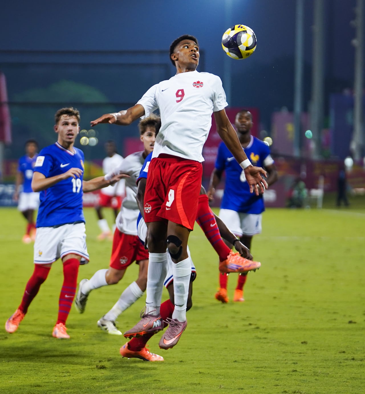 A soccer player representing Canada jumps for the ball. 