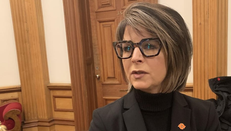 Woman with glasses in a black blazer speaks into a mic while being interviewed.