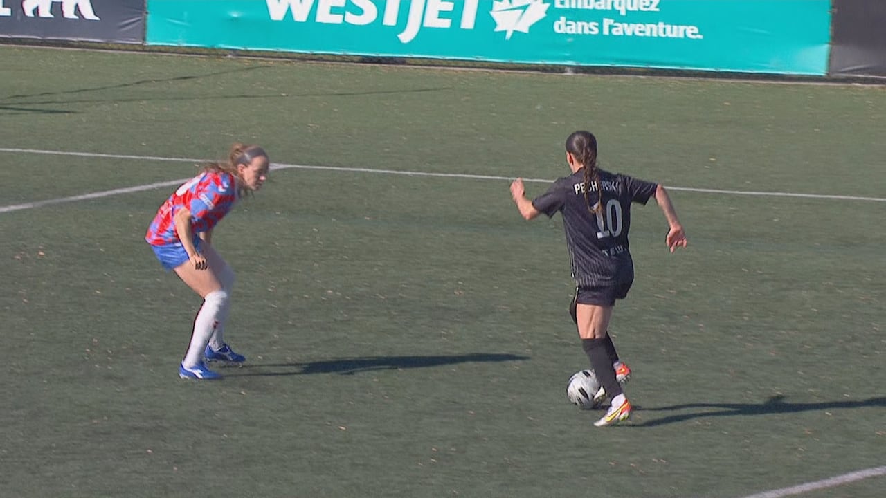 A female soccer player runs with the ball towards a defender.