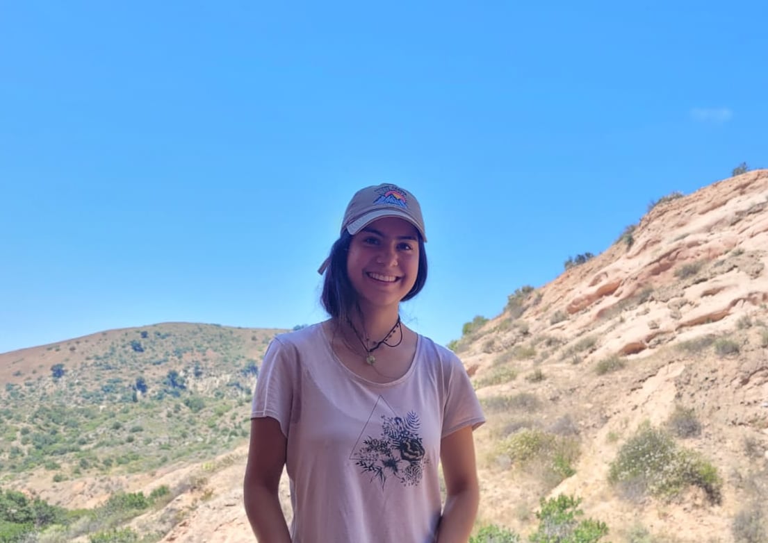 A young woman wearing a ballcap looks into the camera.