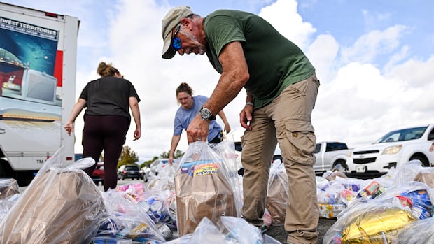 A man picks up a bag with food in it from a pile of bags of food.