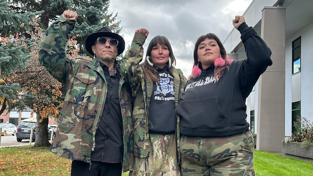 Three Indigenous people stand with their fists in the air.