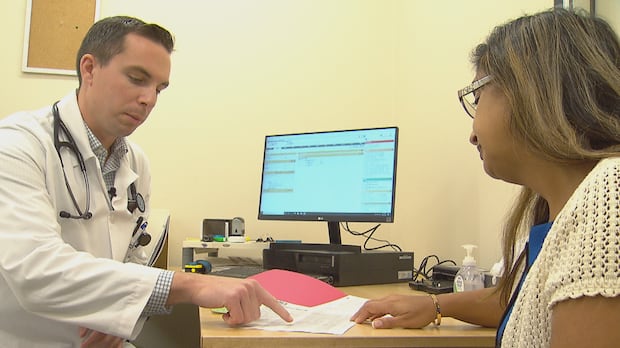 In Manitoba, hundreds of thousands of sick notes are written by doctors every single year. It's something physicians say its wasting valuable ti A man in a white coat points to paperwork while sitting next to a woman
