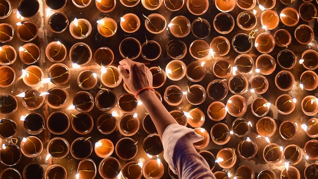 A hand reaching to light rows of earthen lamps at night.
