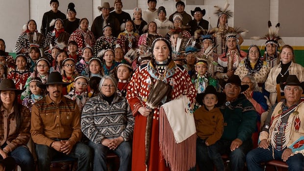 A woman stands in front of a large group of people dressed in brightly coloured clothing.