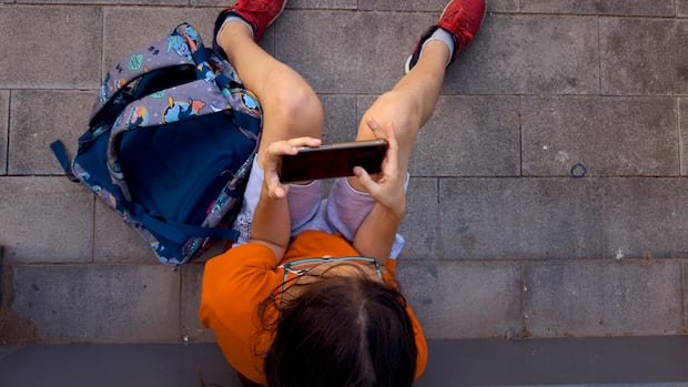 A 11-year-old boy plays with his father's phone outside school in Barcelona, Spain