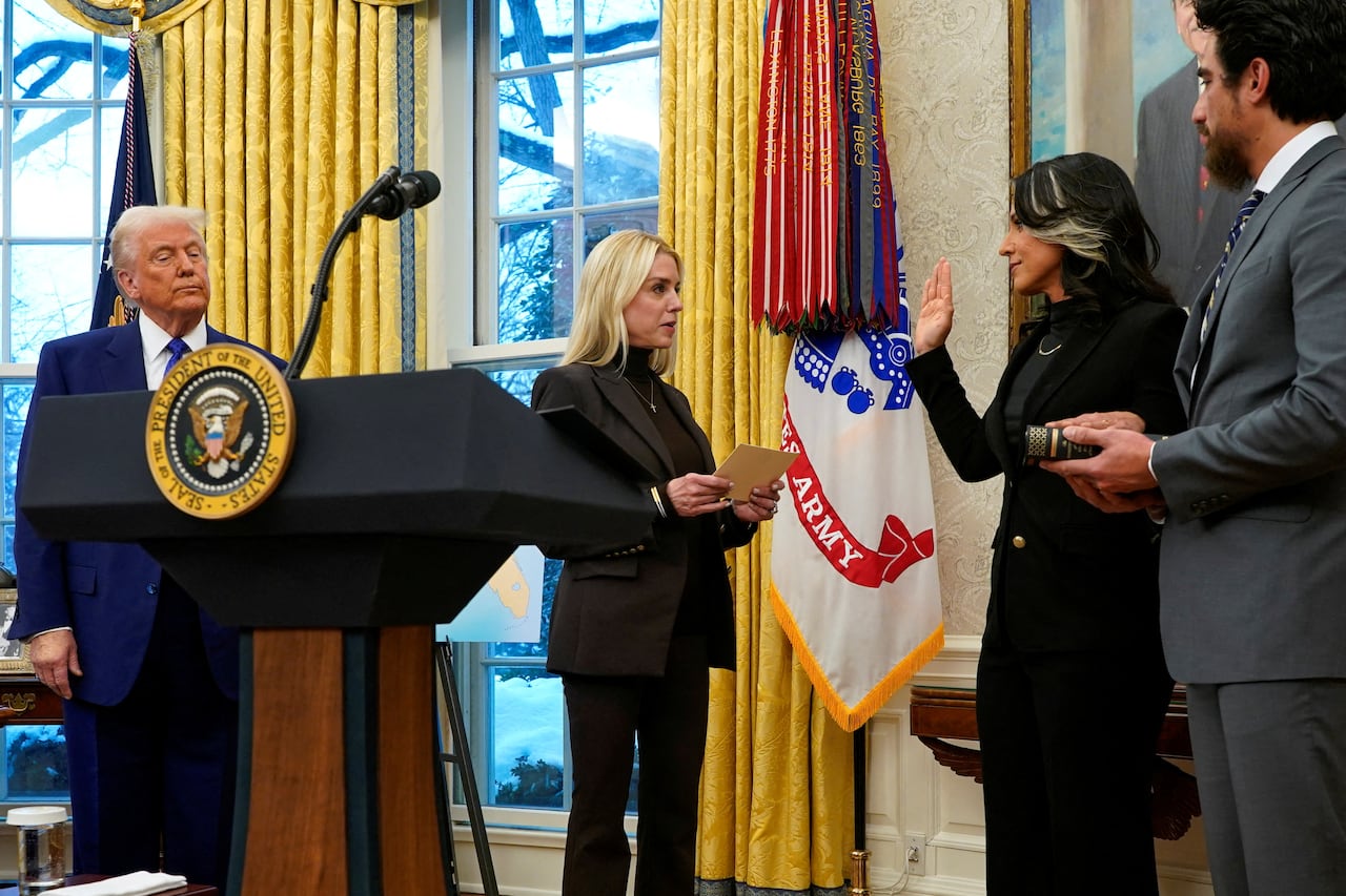 Four people stand in a formal room, one of them swears an oath on a book
