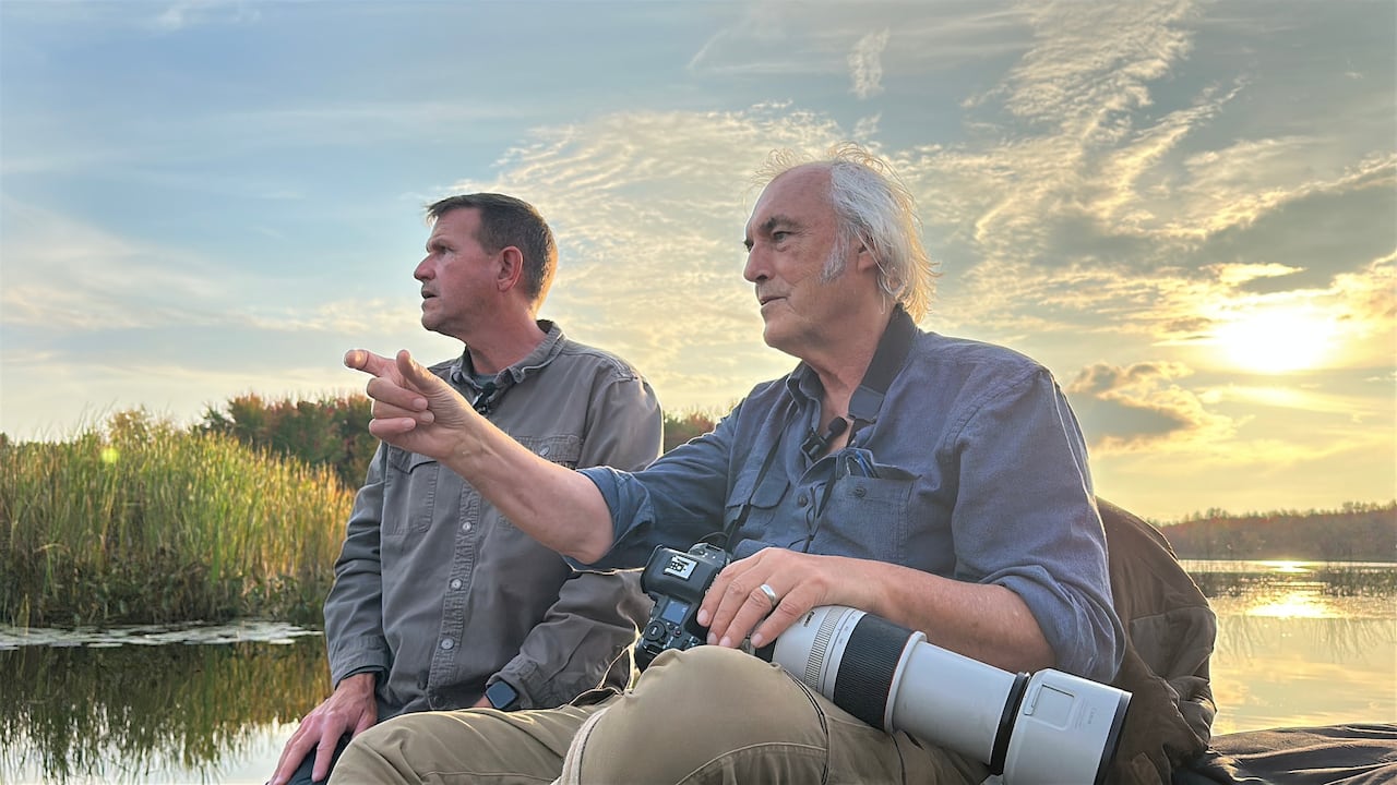 Two men on a boat at sunset, holding a camera with a large lens
