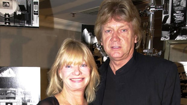 Moody Blues lead singer John Lodge and his wife arrive at the Grosvenor Hotel in London, Oct. 18, 2001. A man and a woman wearing black smile for a camera.