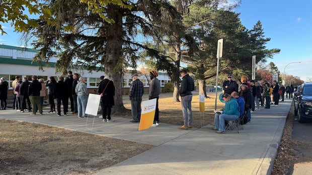 A long line of people waits outside a school to vote. The line snakes around the corner. 
