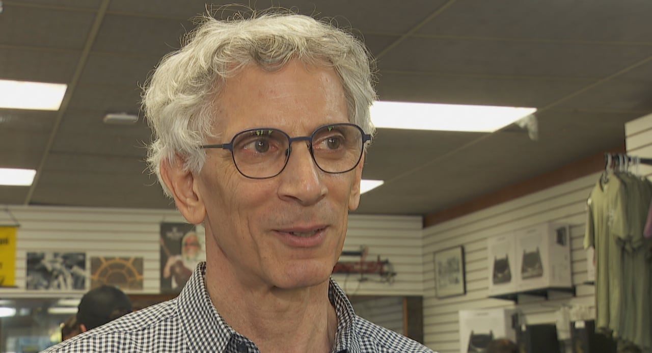 A man wearing glasses looks at the camera. He's wearing a plaid shirt
