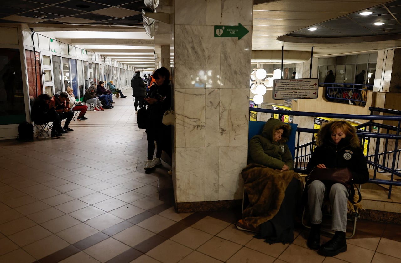 People in winter coats sit and sleep in a Metro station