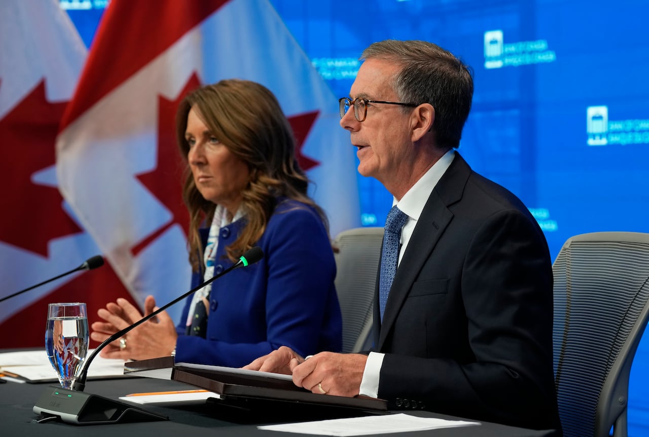 A woman and a man are shown sitting next to each other as they speak during a press conference.