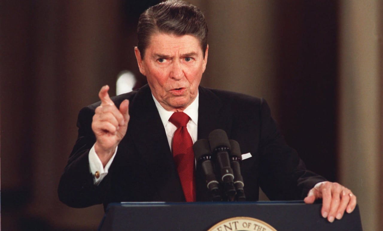 A man in a suit gestures while speaking at a lectern