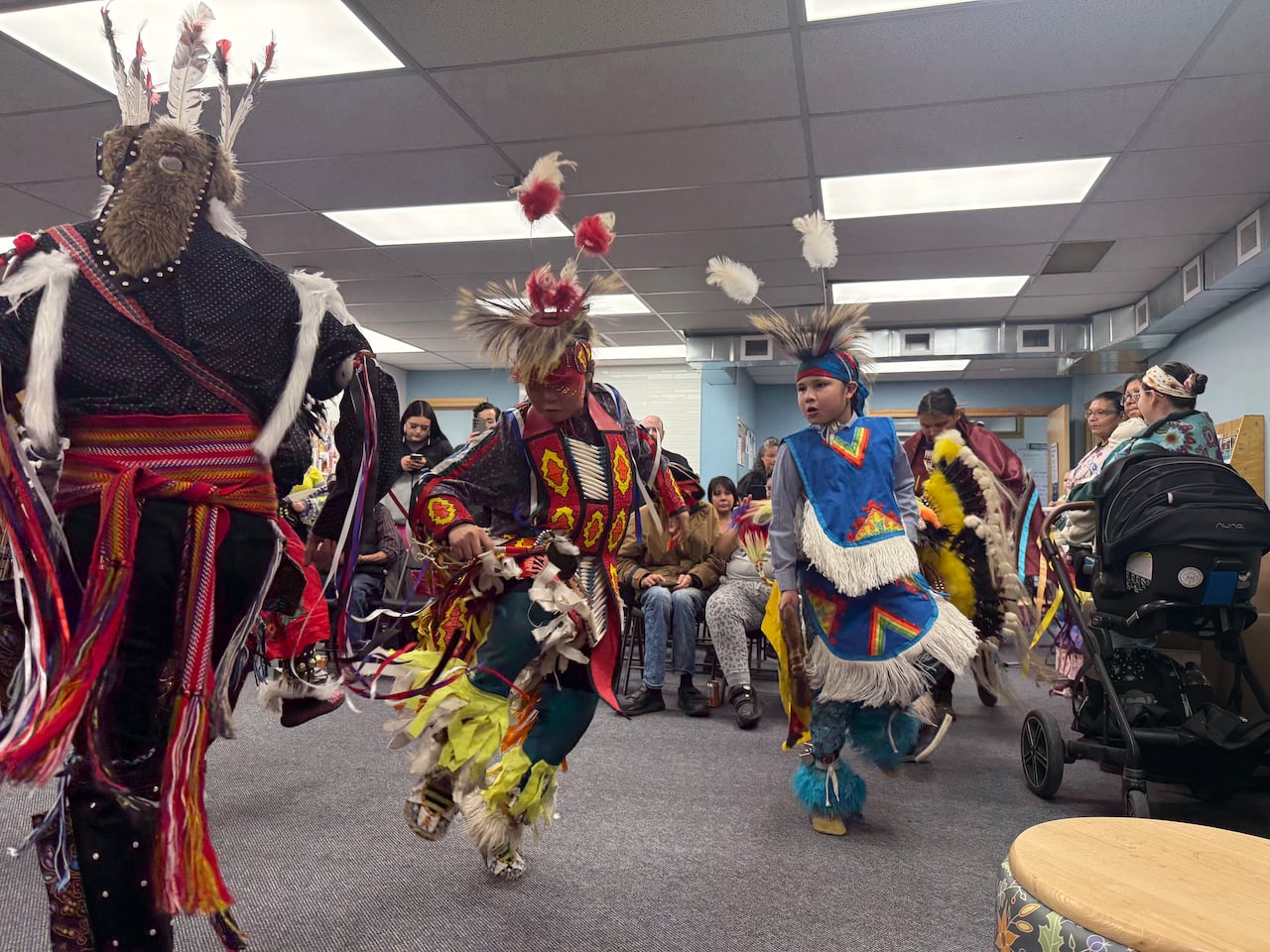 A community of people watching powwow dancers dance in a cultural program.