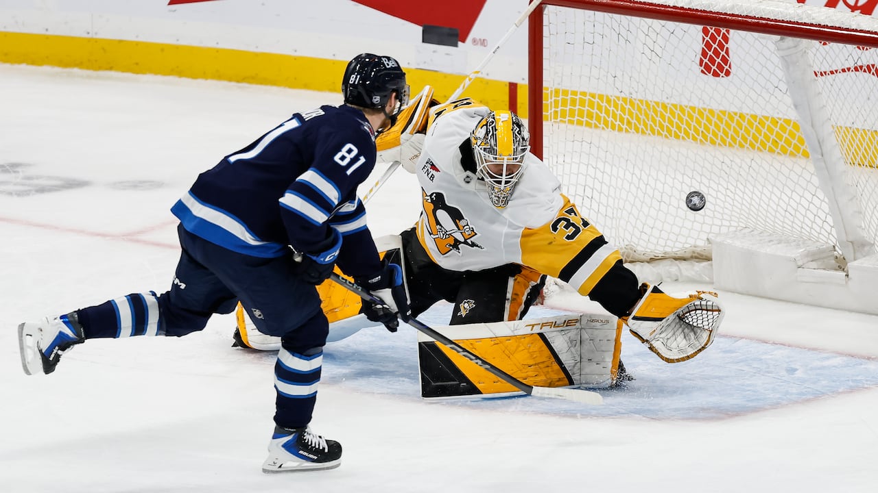 A hockey subordinate shoots a puck into the nett arsenic a goalie reaches to effort to marque a save.