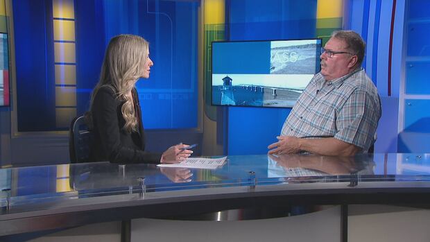 P.E.I. Shellfish Association president Bob MacLeod talks with Sheehan Desjardins on the Compass set. A woman with long blonde hair talks with an older man in glasses wearing a light plaid shirt.