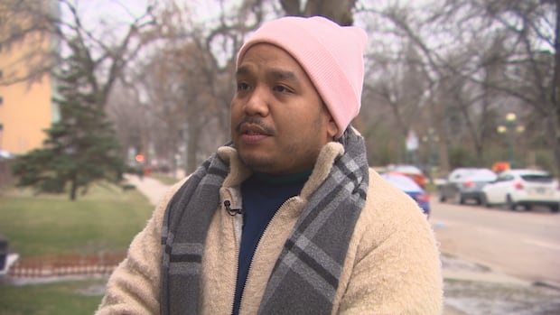 A man in a brown jacket wearing a pink toque standing outside