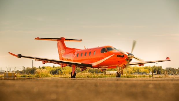 A small plane painted orange is parked on a runway