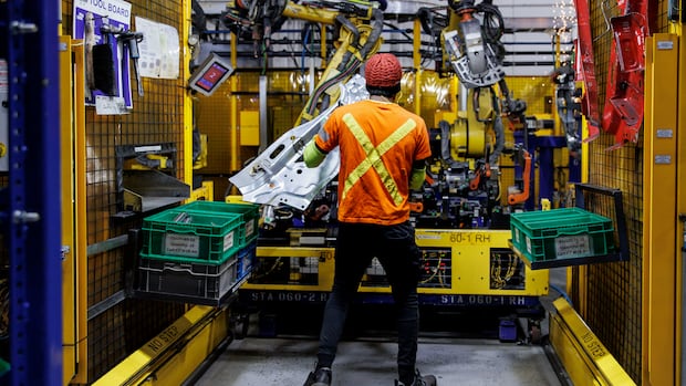 A worker uses a machine to stamp out vehicle components at Martinrea auto parts, in Woodbridge, Ont., on Feb. 3, 2025. A worker in a fluorescent shirt is shown from behind working with a large machine.