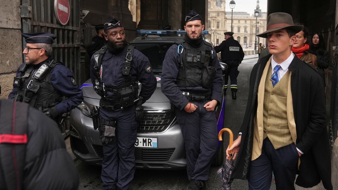 A man in a suit and fedora walks past police officers