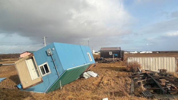 A light-blue colored trailer is shown tipped over in a rural setting.