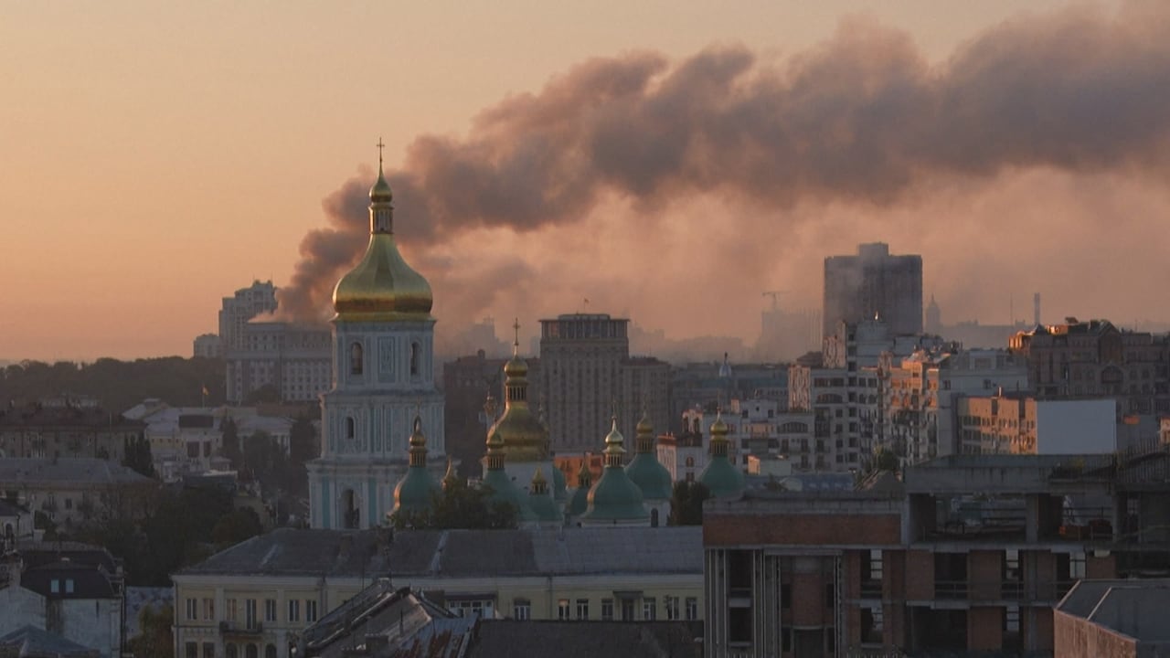 Skyline of buildings in Russia in the foreground. Grey smoke billowing against the pink and orange sky in the background