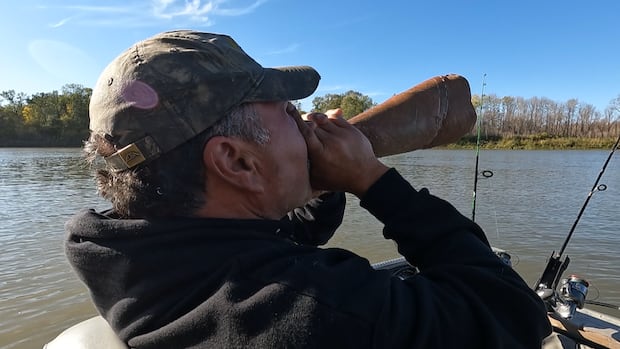 A man sitting in a boat on the water holds a cone to his mouth.