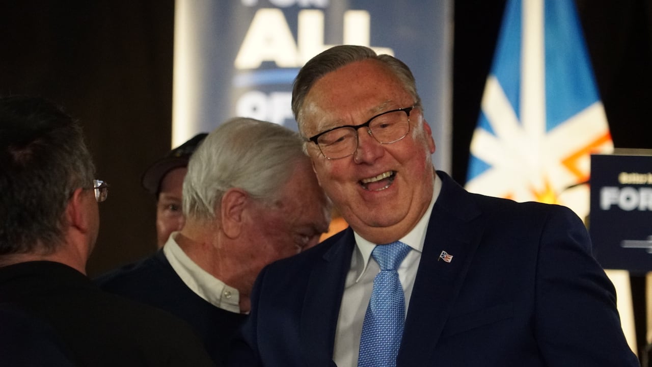 A man wearing a suit and glasses smiles broadly.